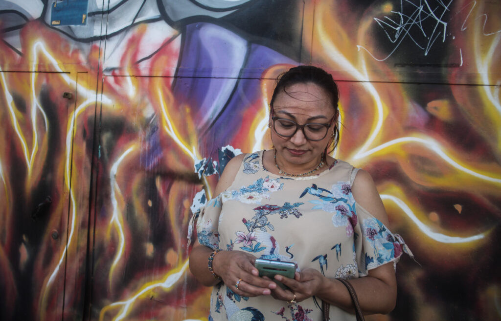 Silmälasipäinen nainen tutkii känykkää, taustalla graffitiseinä